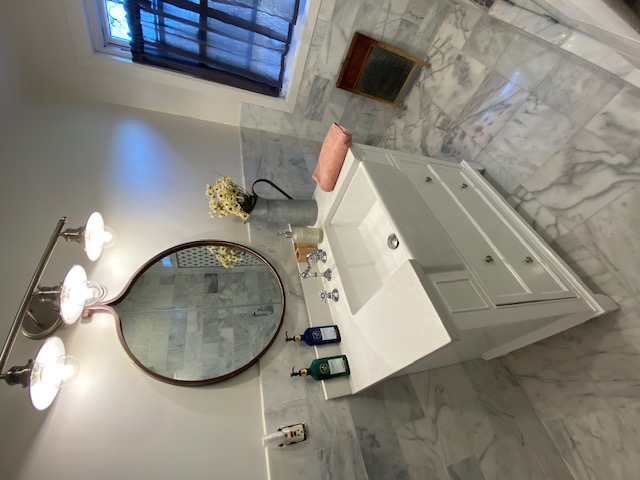 Bathroom after — white vanity with round mirror and marble countertop